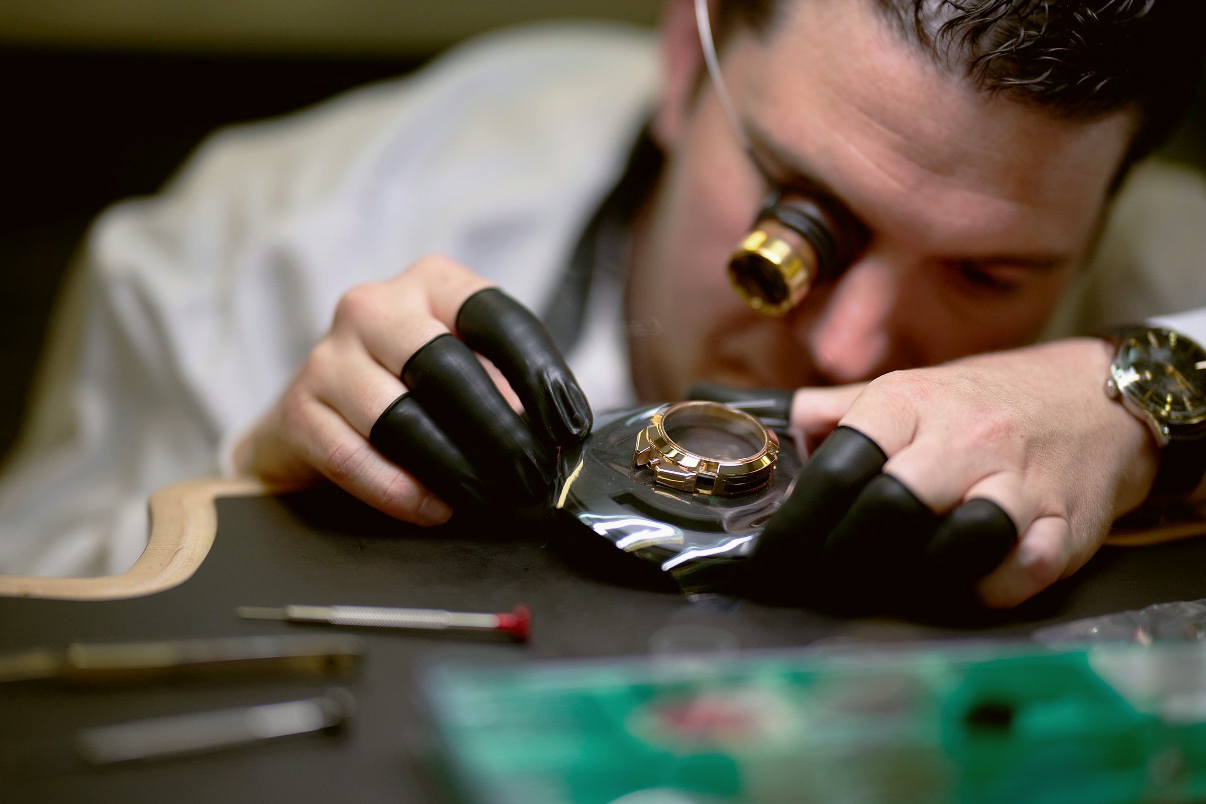 Watchmaker inspecting a gold case under a loupe