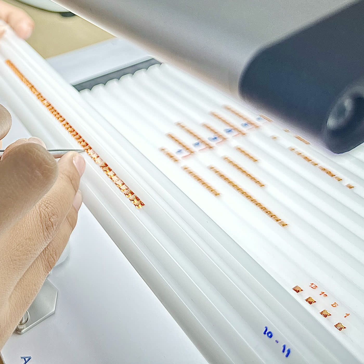 NIRU sorter ordering orange-red sapphires into the grooves of a color-matching tray, with reference parcels of matched stones laid out alongside under a polariscope