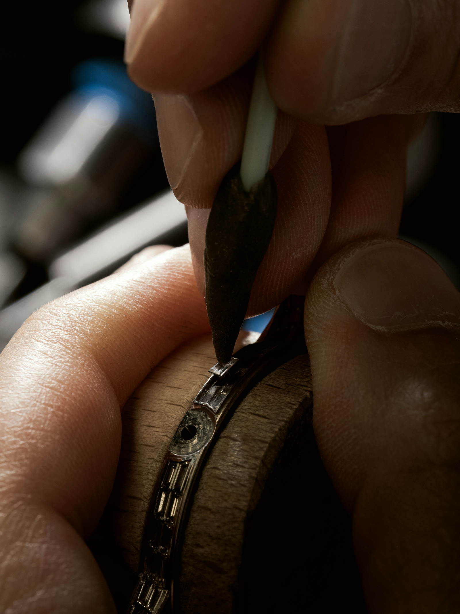Stone setter pressing a row of baguette diamonds on a watch bezel held on a wooden mandrel