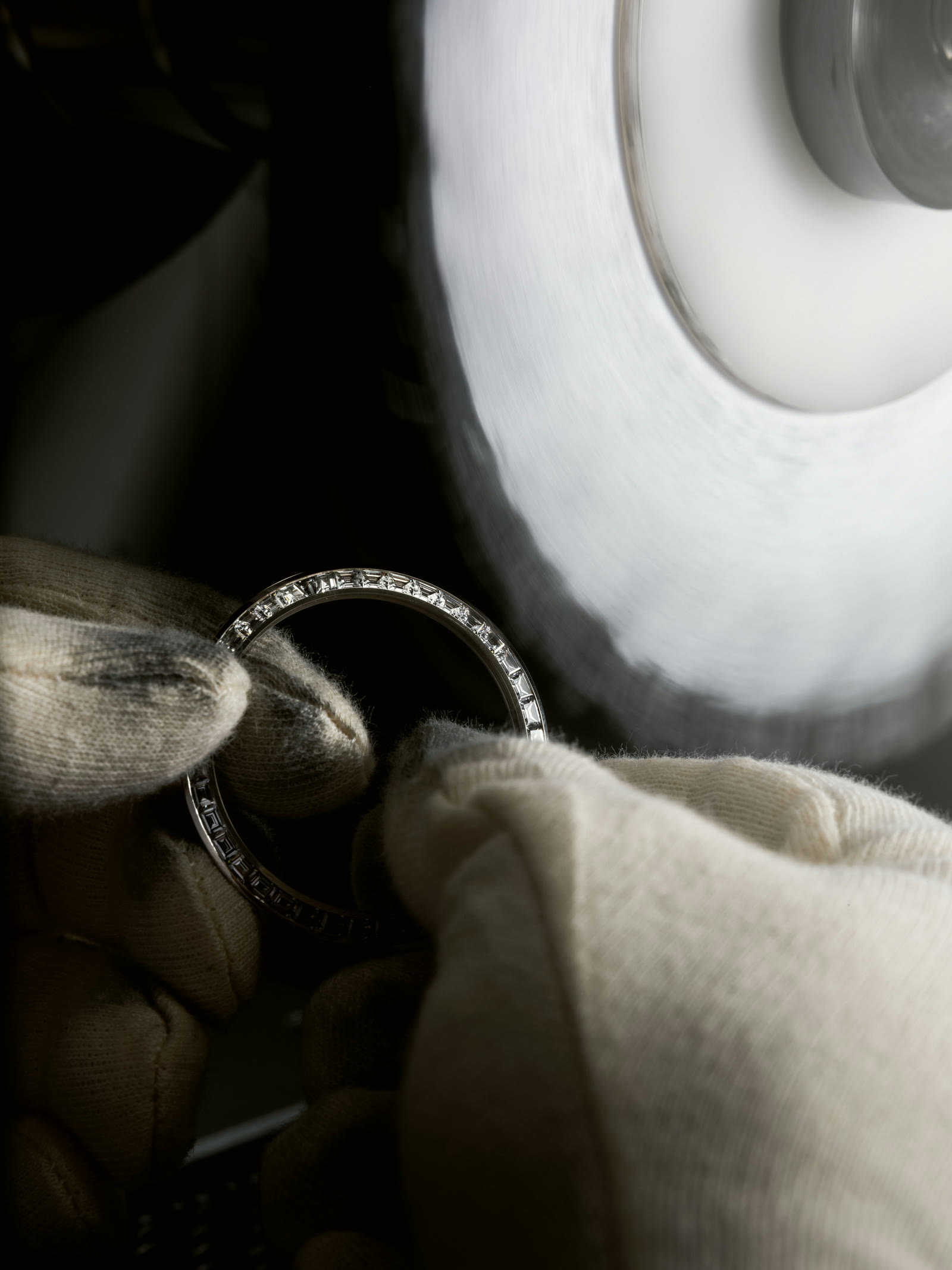 Gloved hands holding a baguette-set ring at the polishing wheel