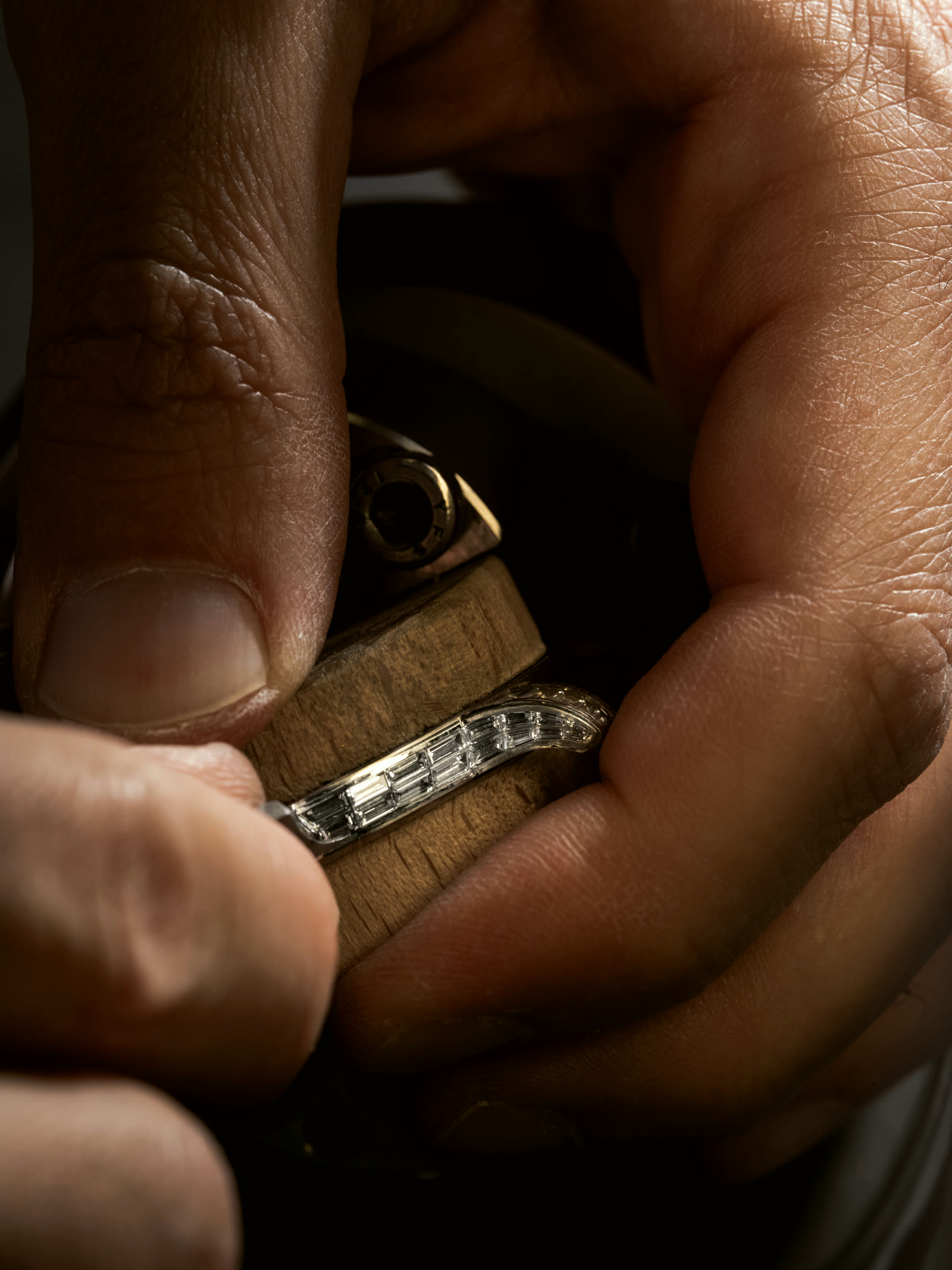 Setter's hands adjusting a fully set baguette bezel on the wooden mandrel