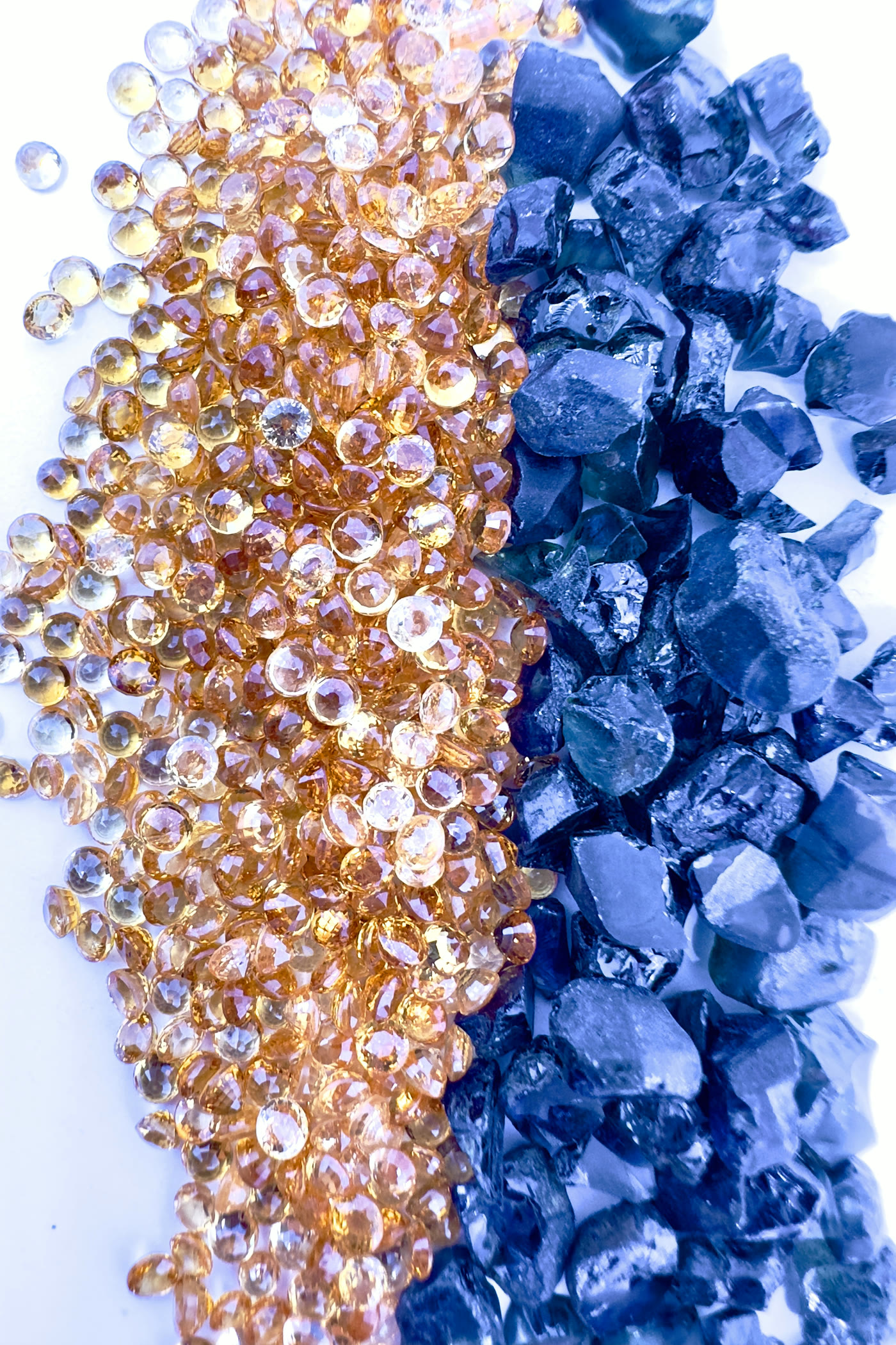 Split composition of orange and blue colored stones: faceted round sapphires next to rough sapphire crystals