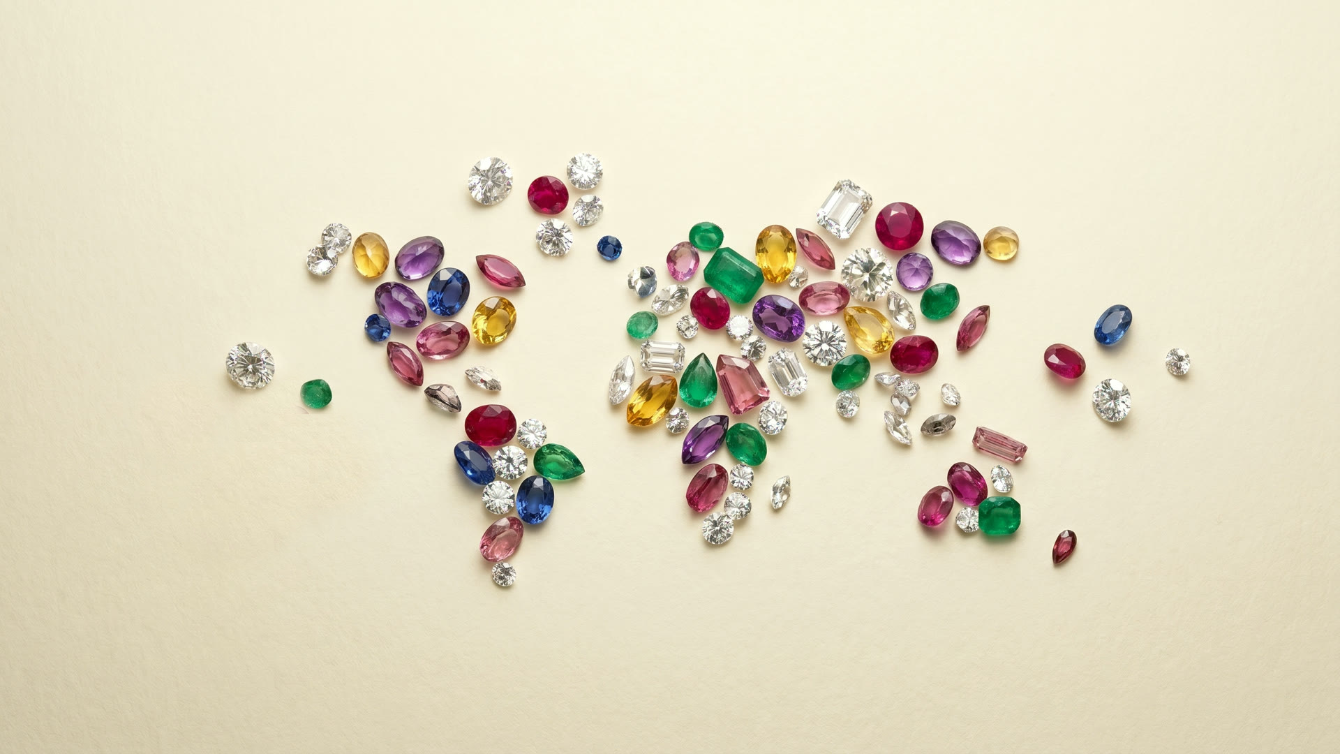 Polished diamonds and faceted multi-color gemstones scattered on warm cream paper, soft studio light