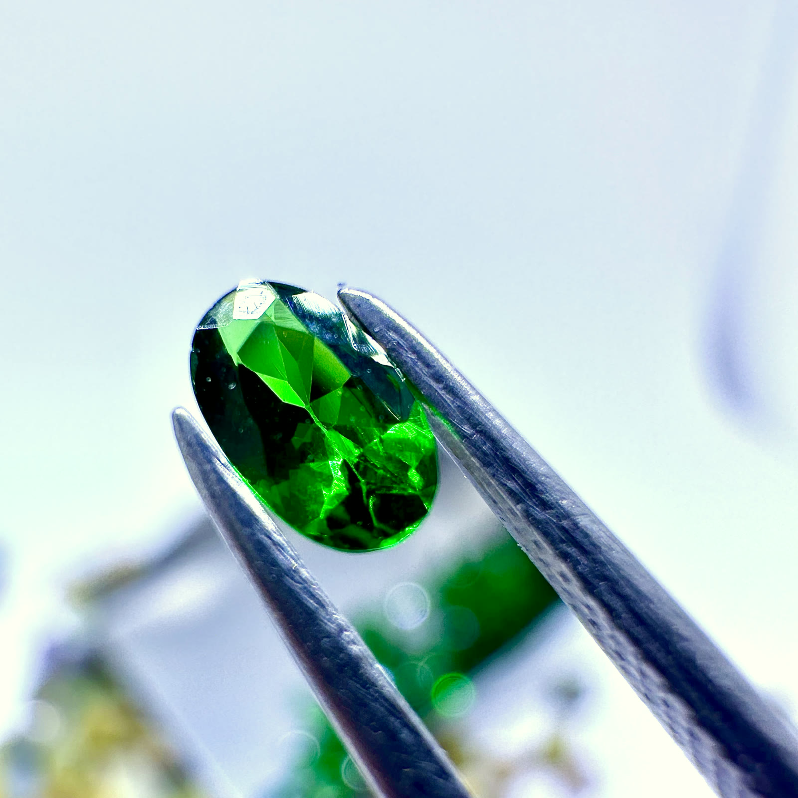 A green colored stone held in tweezers during gemmological examination