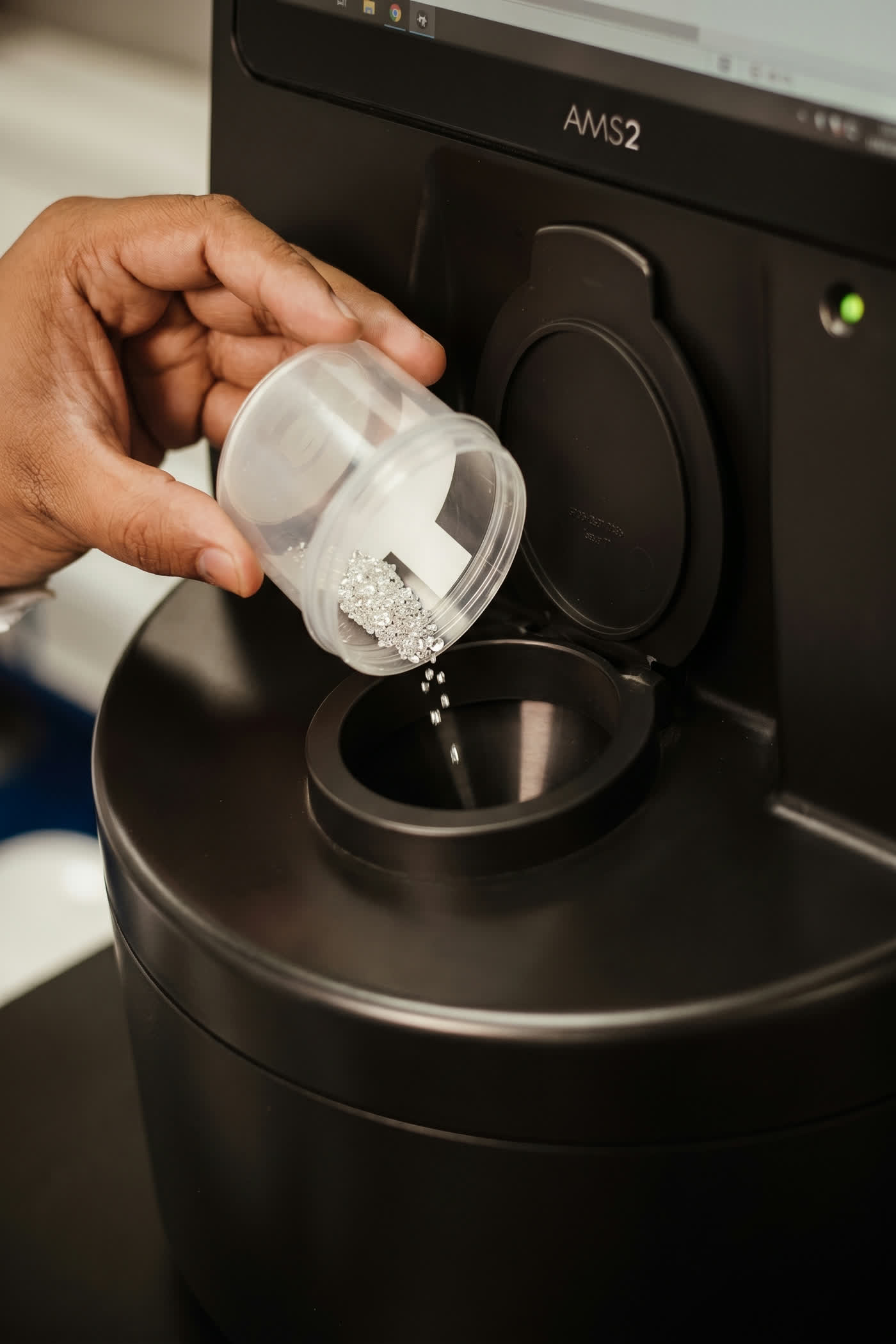 A hand pouring diamonds into a De Beers AMS2 screening instrument in a NIRU laboratory