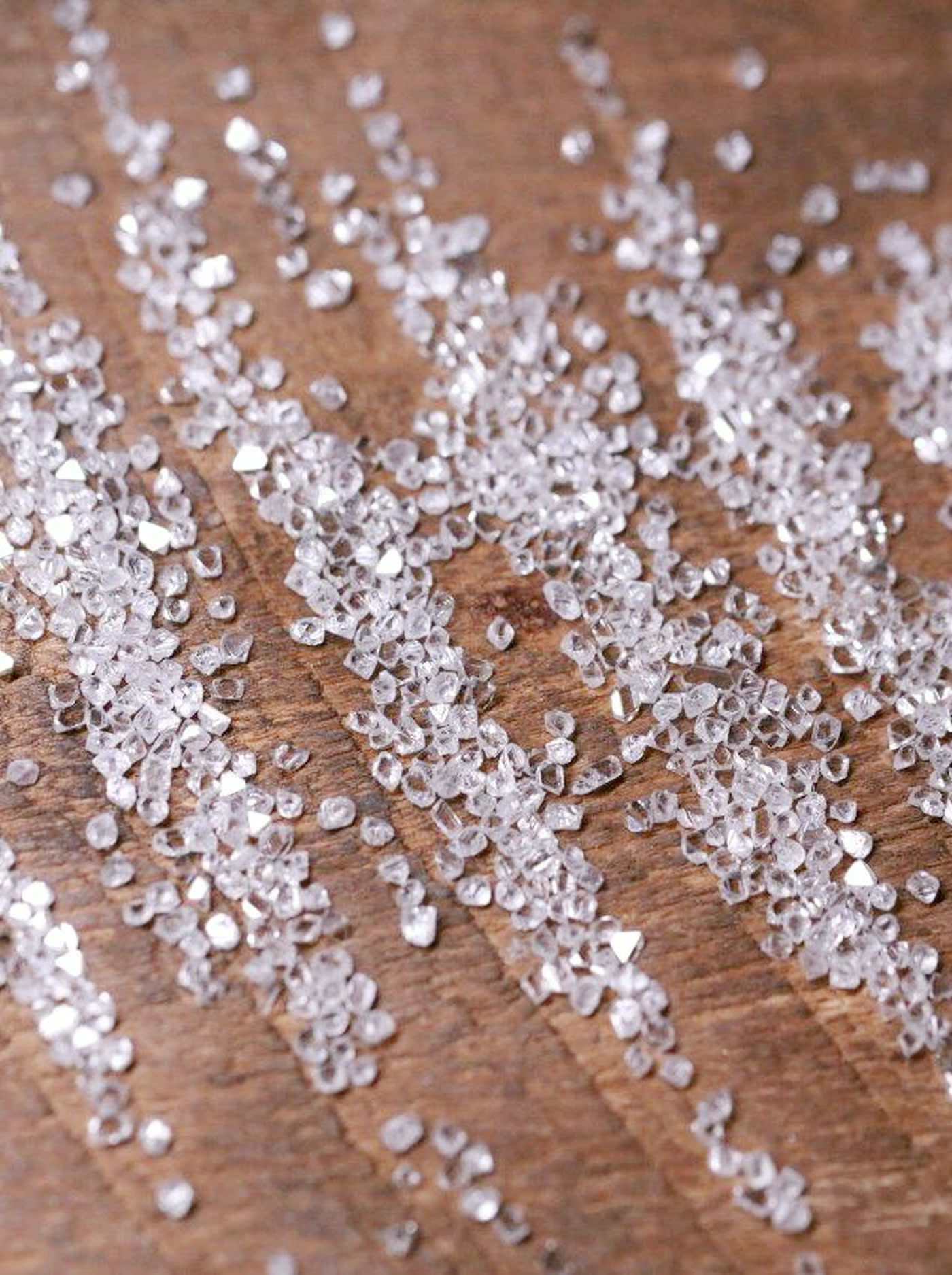 Small rough natural diamond crystals scattered on a wooden surface, before entering the manufacturing process