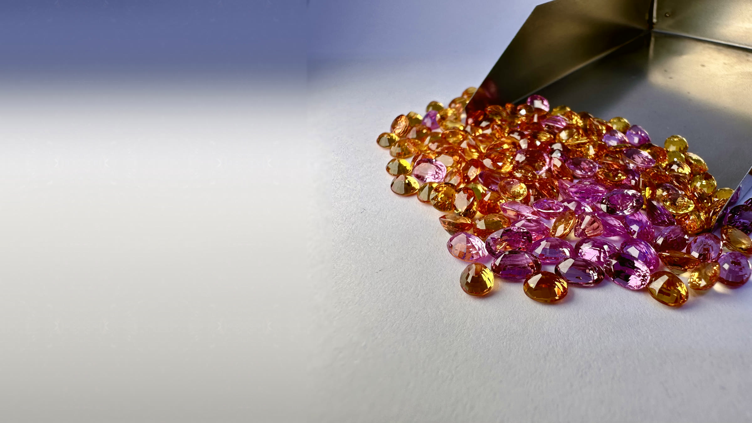 Polished pink, orange and yellow sapphires poured onto a pale working surface