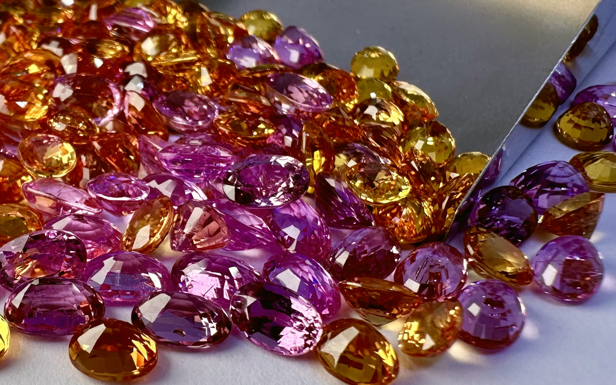 Polished pink, orange and yellow sapphires poured onto a pale working surface