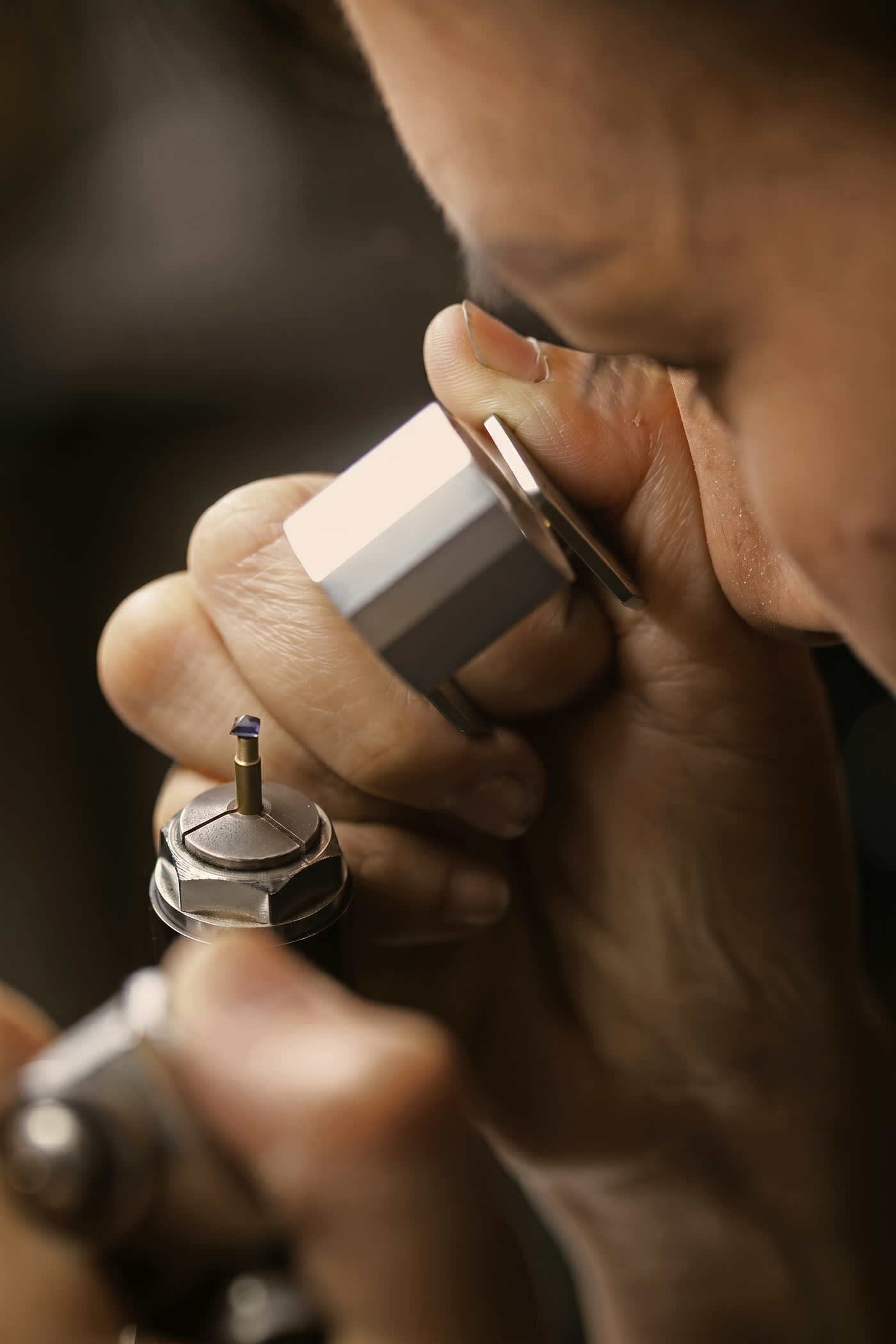 NIRU craftsman on the faceting line examining a blue sapphire on a dop stick with a jeweler's loupe